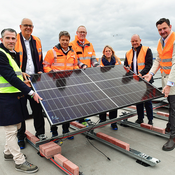 Der Vorstand und weitere Menschen in Schutzanzügen halten eine Solarpanele (Foto)