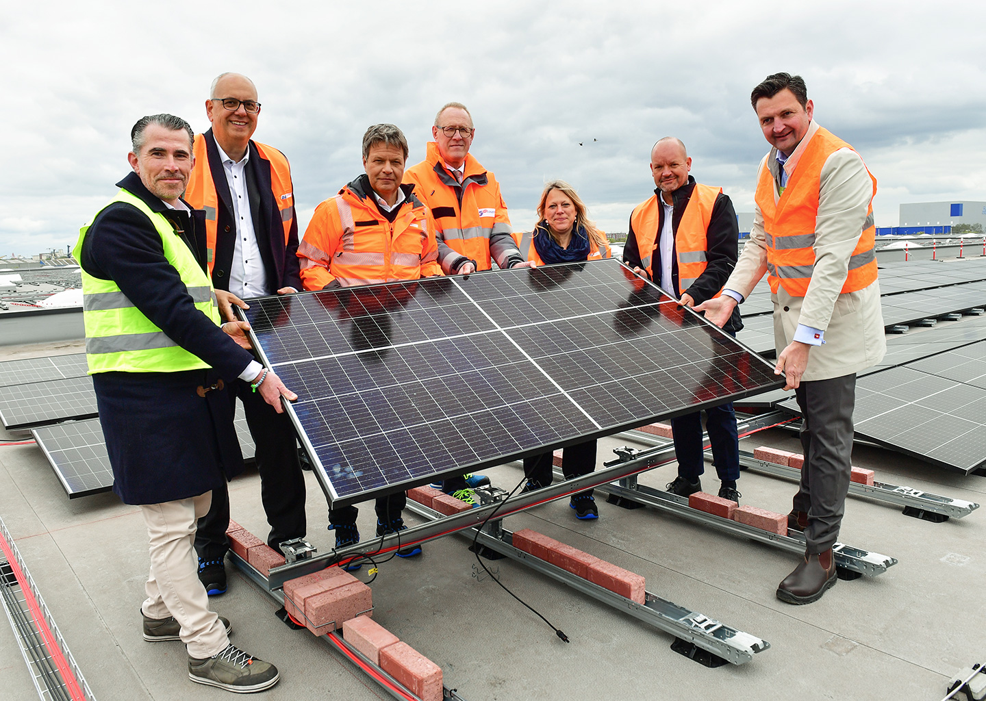 Der Vorstand und weitere Menschen in Schutzanzügen halten eine Solarpanele (Foto)