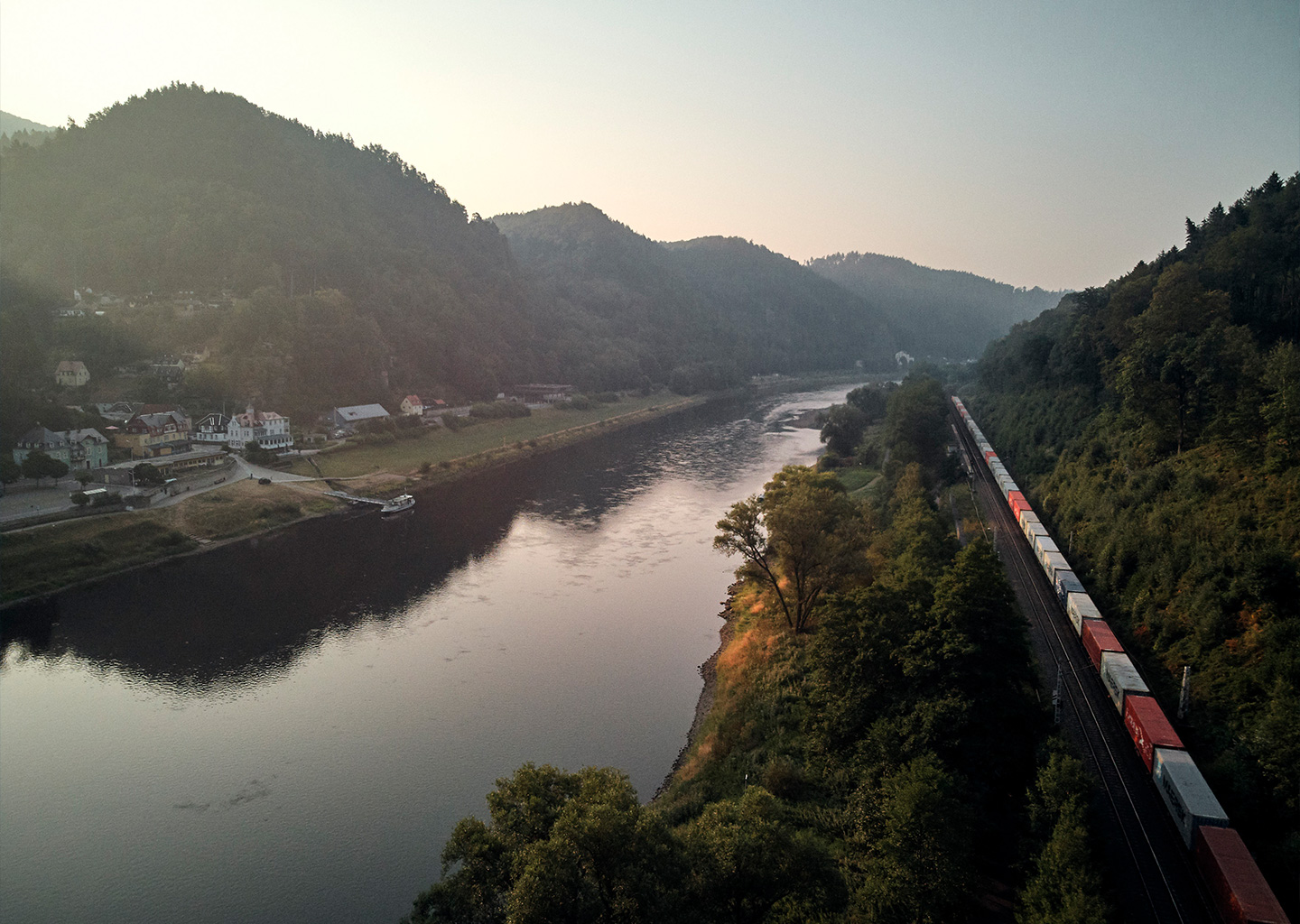 Ein Zug fährt an einem Fluss entlang durch eine Landschaft (Foto)