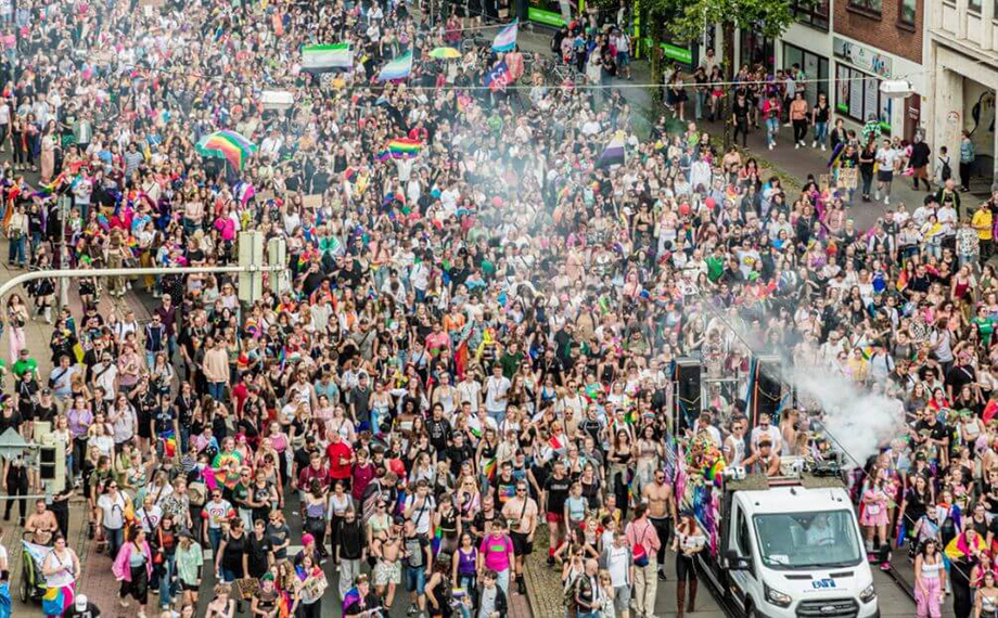 Ein Foto einer Parade am Christopher Street Day mit vielen Menschen mit Regenbogenflaggen (Foto)