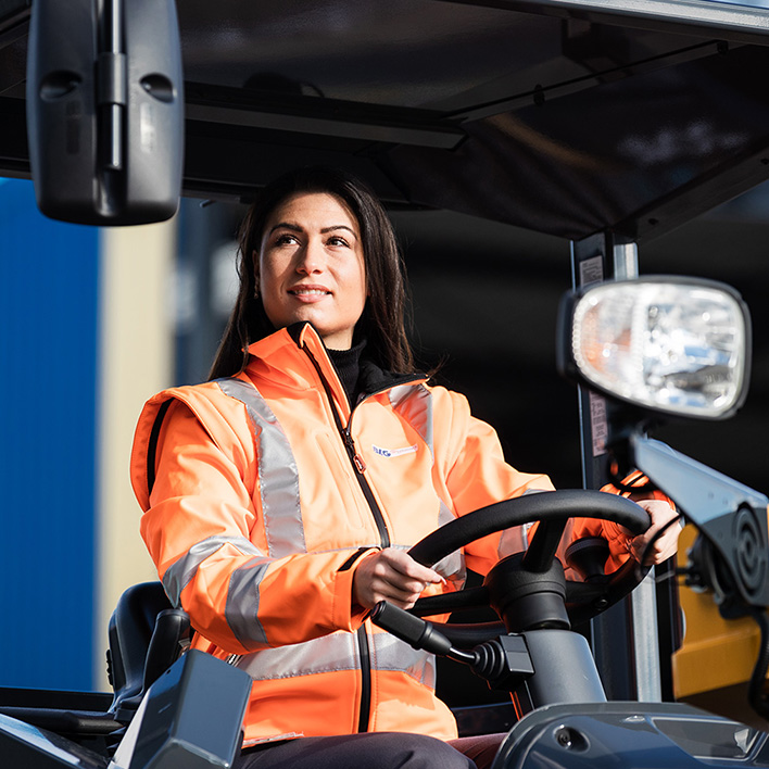 A woman in protective gear with brown hair is driving a forklift (Photo)