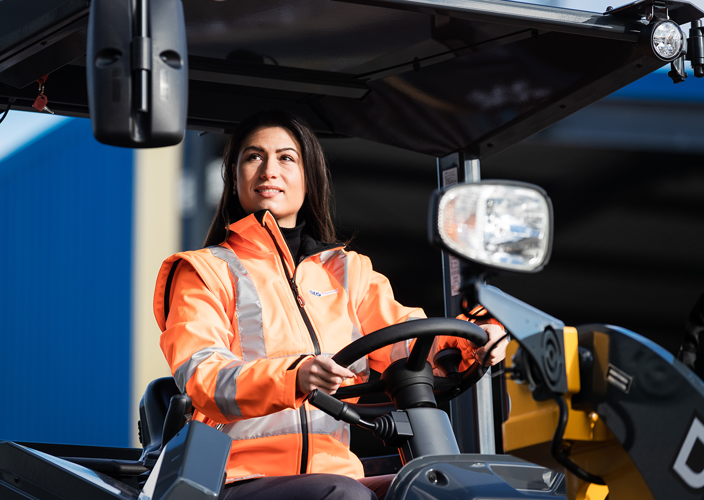 A woman in protective gear with brown hair is driving a forklift (Photo)