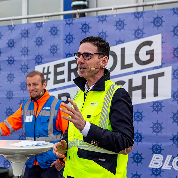 Matthias Magnor speaks in a yellow protective vest, a man stands in the background and smiles (Photo)