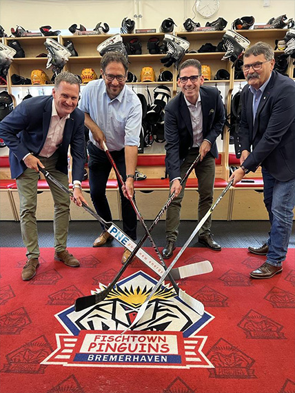 Four people holding ice hockey sticks, the logo of the Fischtown Penguins Bremerhaven can be seen (Photo)