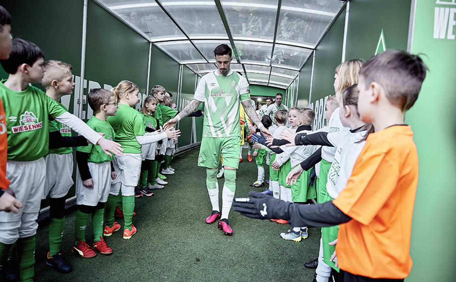 A soccer player from SV Werder Bremen runs through a corridor and high-fives with children standing on the sidelines (Photo)