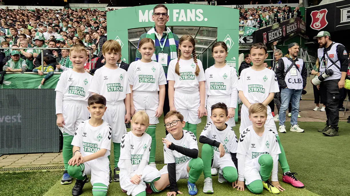 Matthias Magnor, Geschäftsführer der BLG, mit Kindern, die in einem Stadion Weder Strom-Trikos tragen (Foto)