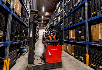 Red forklift moving between tall warehouse shelves in a storage facility